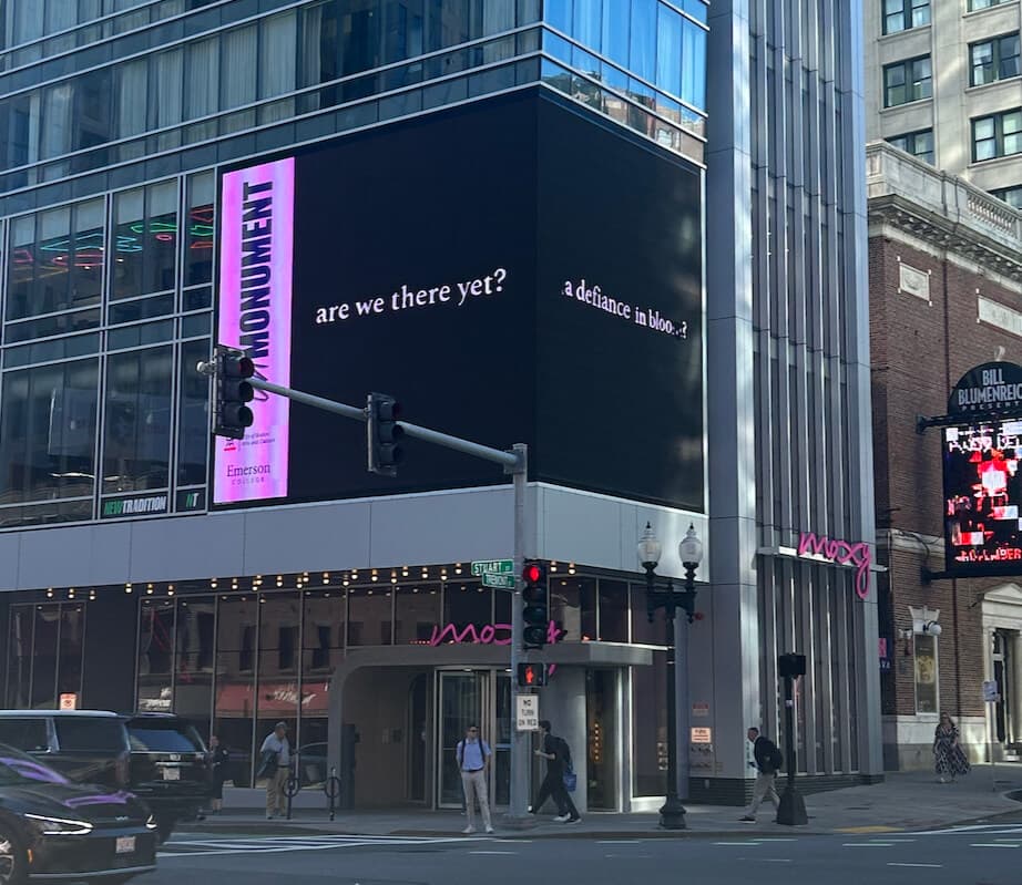 A black advertising screen on a high-rise that says "are we there yet?"